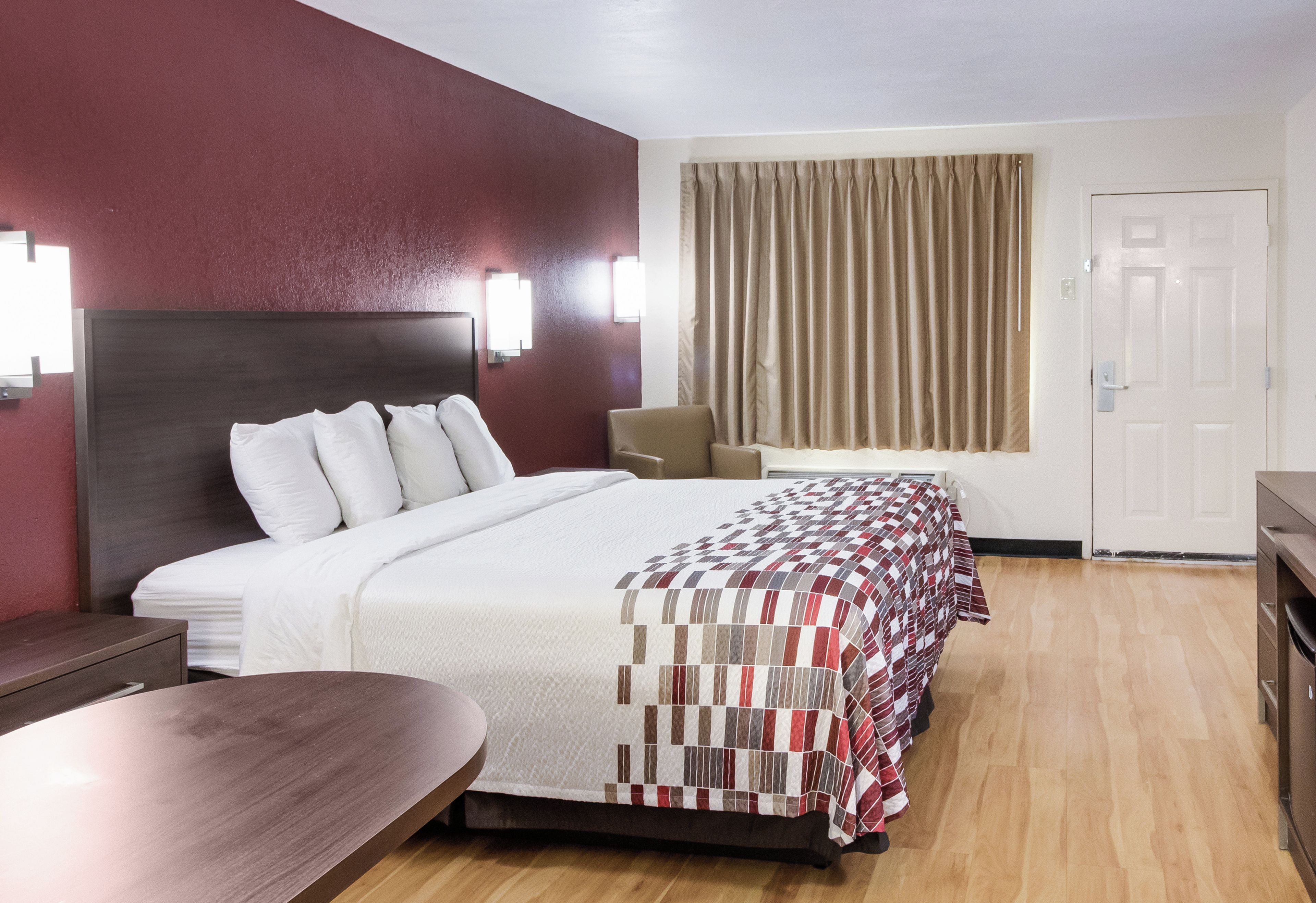 Habitación de hotel con cama, escritorio, silla, armario y ventana con cortinas.