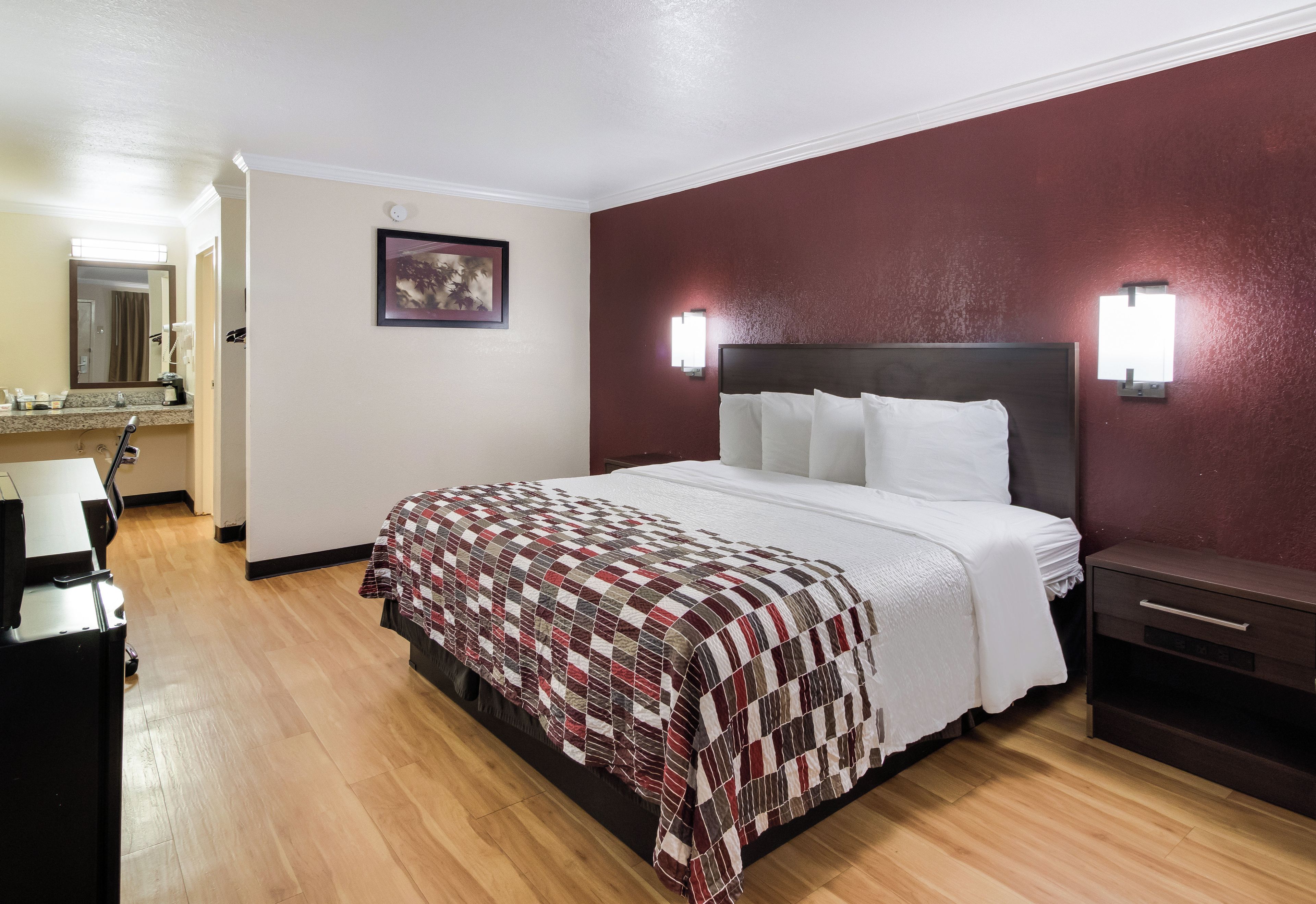 Une chambre d’hôtel avec un lit, un bureau, une chaise, un miroir et un tableau au mur.