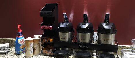 Una encimera de cocina con una cafetera, una botella de Nestlé Coffee Mate, un recipiente con crema para café y una cafetera Bunn.