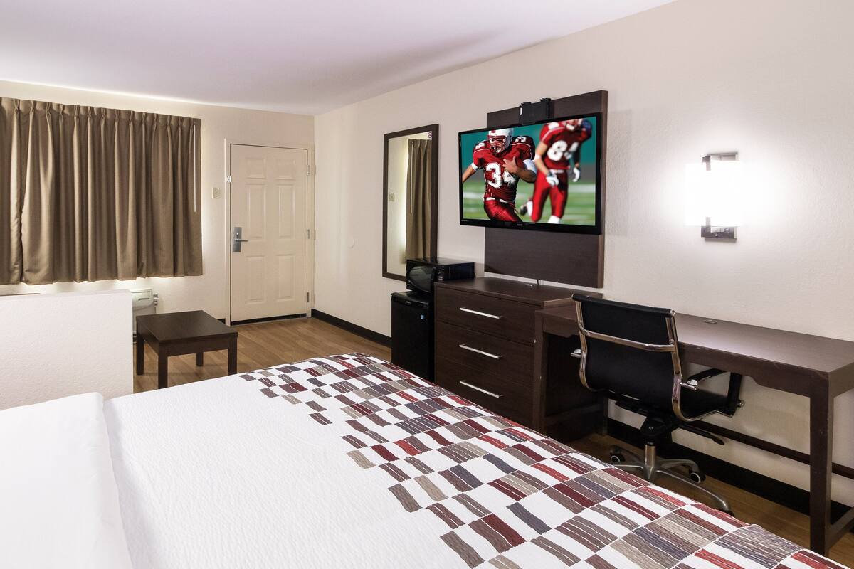A hotel room with a bed, a desk, a chair, a television, and a mirror.