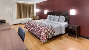 A hotel room with a bed, a desk, a chair, a nightstand, and a window with curtains. - Red Roof Inn & Suites Commerce - Athens (Commerce)