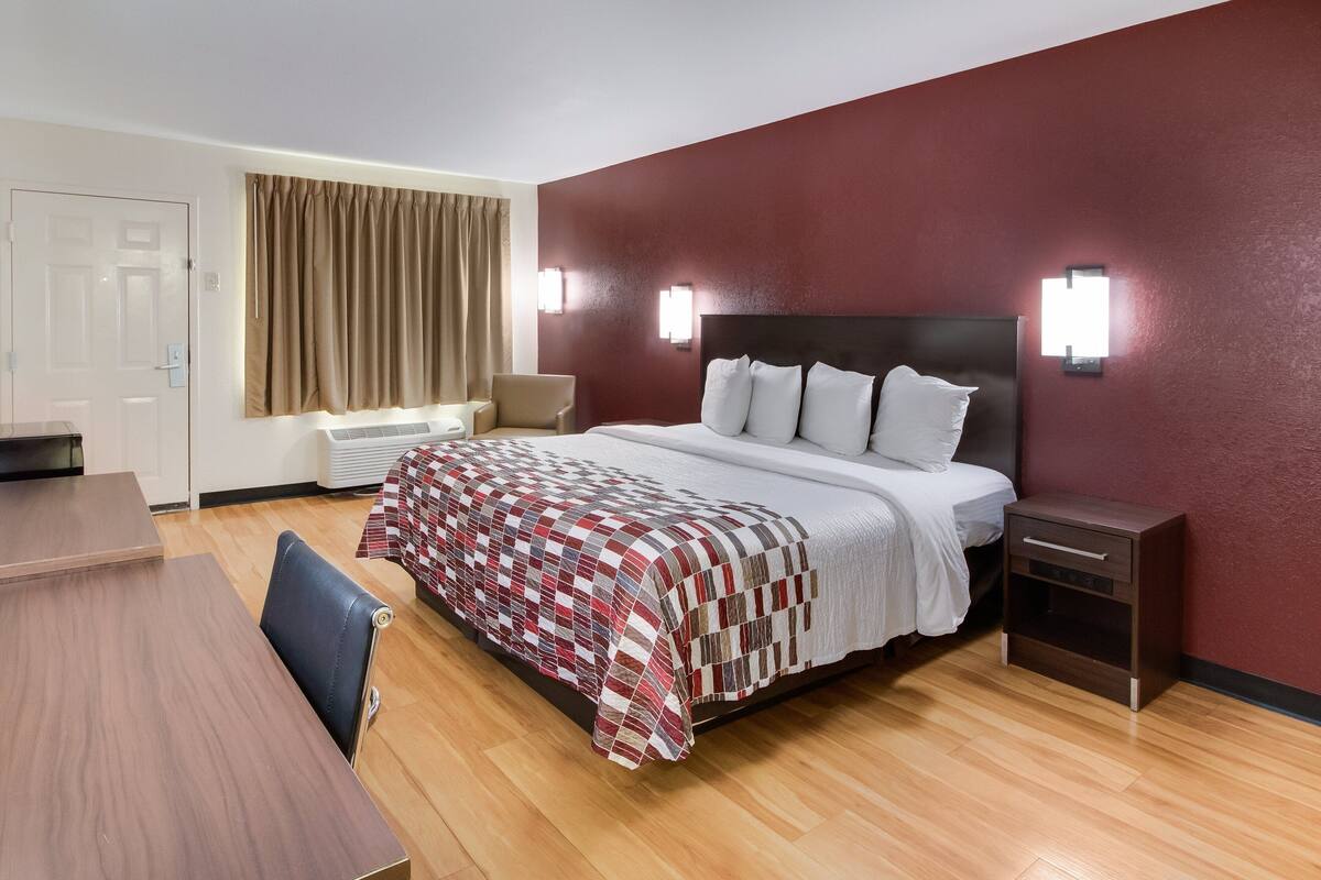 A hotel room with a bed, a desk, a chair, a nightstand, and a window with curtains.