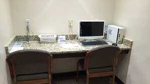 A small office space with two wooden chairs, a desktop computer, and a monitor. There are two power outlets on the wall, and a telephone on the desk. - Red Roof Inn & Suites Commerce - Athens (Commerce)