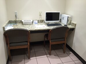 A small office space with two wooden chairs, a desktop computer, and a monitor. There are two power outlets on the wall, and a telephone on the desk. - Red Roof Inn & Suites Commerce - Athens (Commerce)
