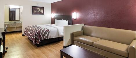 A hotel room with a bed, a sofa, a coffee table, a desk, and a mirror.