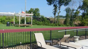 An outdoor seating area with metal chairs and a table, a red railing, and a grassy area with trees and a distant building. - Red Roof Inn & Suites Commerce - Athens (Commerce)