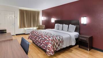 A hotel room with a bed, bedside table, lamp, and a desk with a chair.