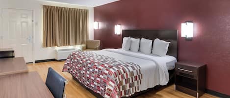 Habitación de hotel con cama, mesita de noche, lámpara y escritorio con silla.