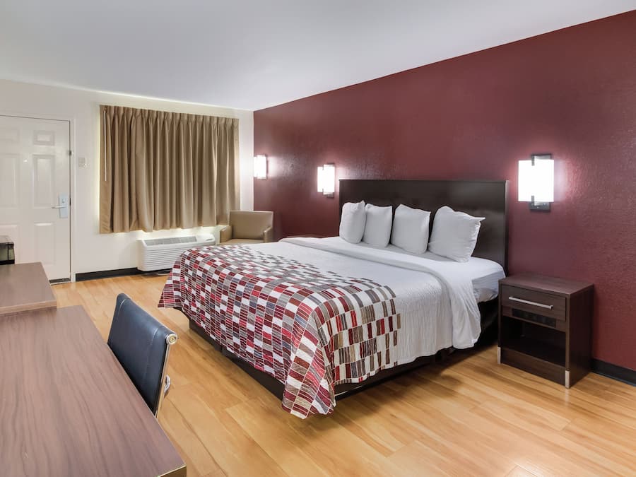 A hotel room with a bed, bedside table, lamp, and a desk with a chair.