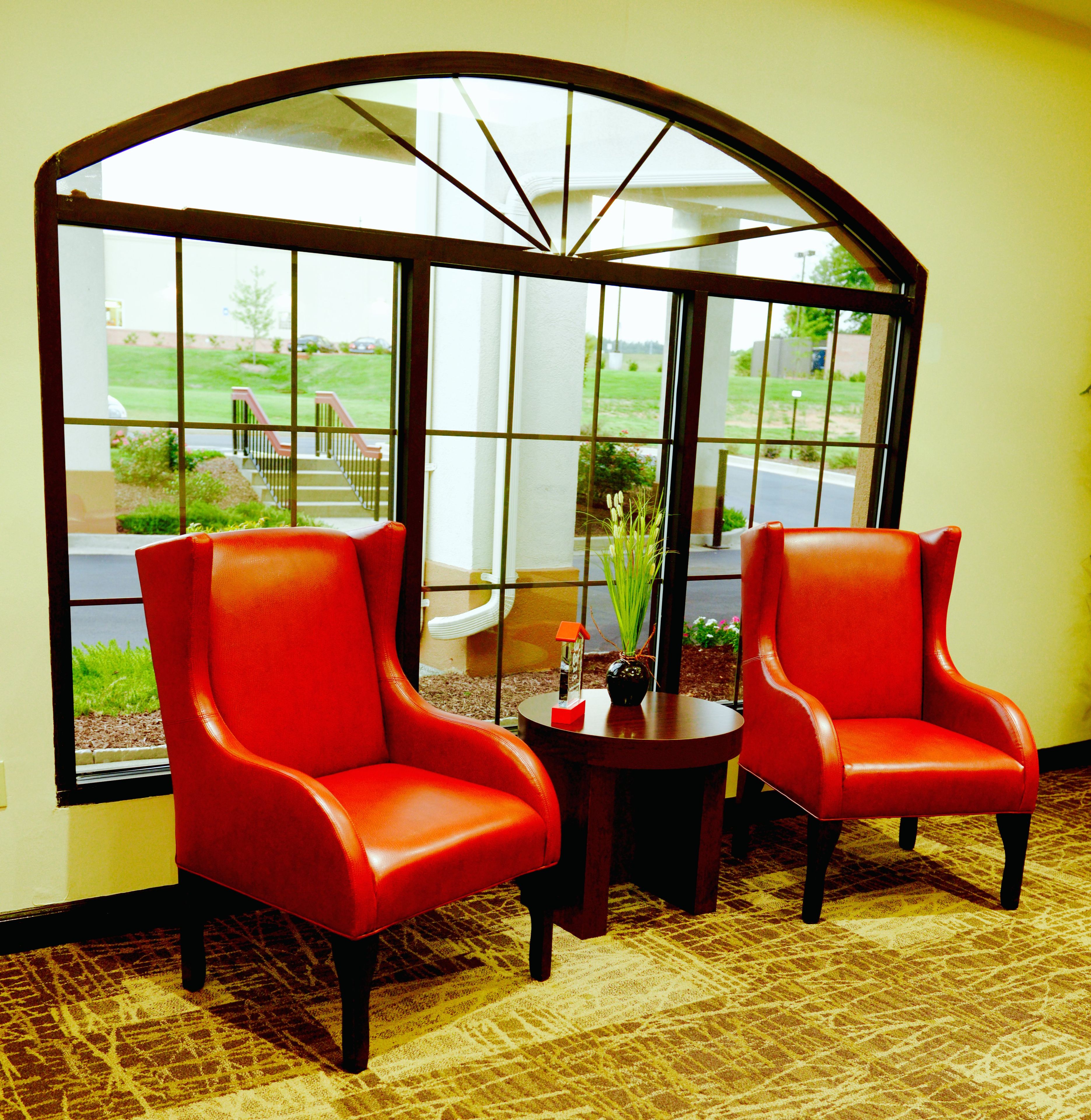 Two red chairs facing a large window with a view of a building and a lawn.