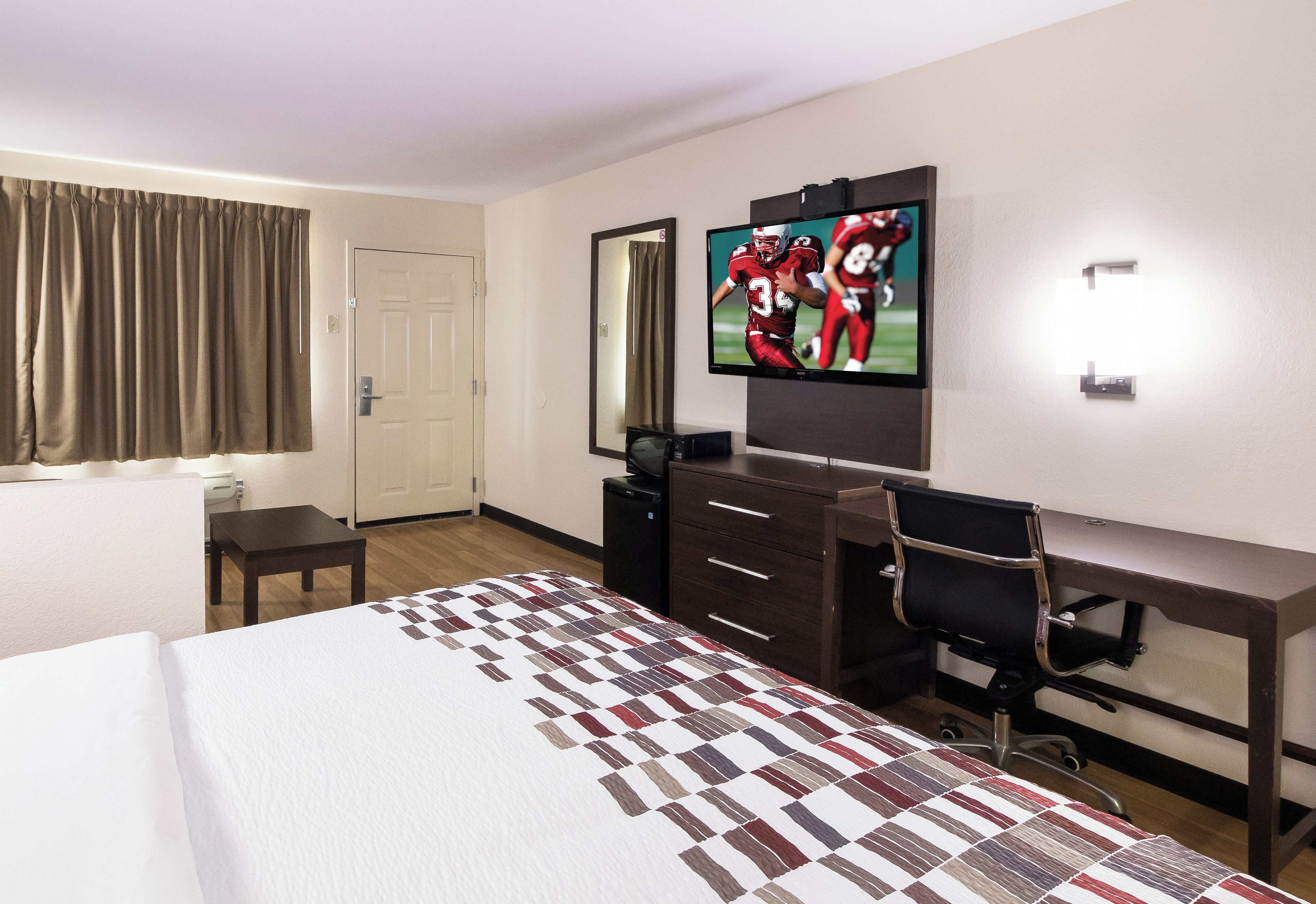 Una habitación de hotel con cama, escritorio, silla, televisor y puerta.