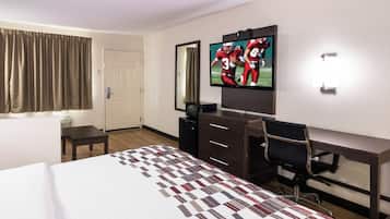 A hotel room with a bed, a desk, a chair, a television, and a door.