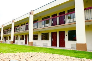 A multi-story motel with a row of rooms, each with a balcony and a red door. - Red Roof Inn & Suites Commerce - Athens (Commerce)