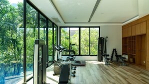 A modern gym with exercise equipment, large windows, and a view of a swimming pool. - Avani Ao Nang Cliff Krabi Resort (Krabi)
