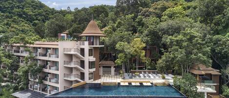 A hotel with a rooftop infinity pool, multiple balconies, and lush surrounding forest.