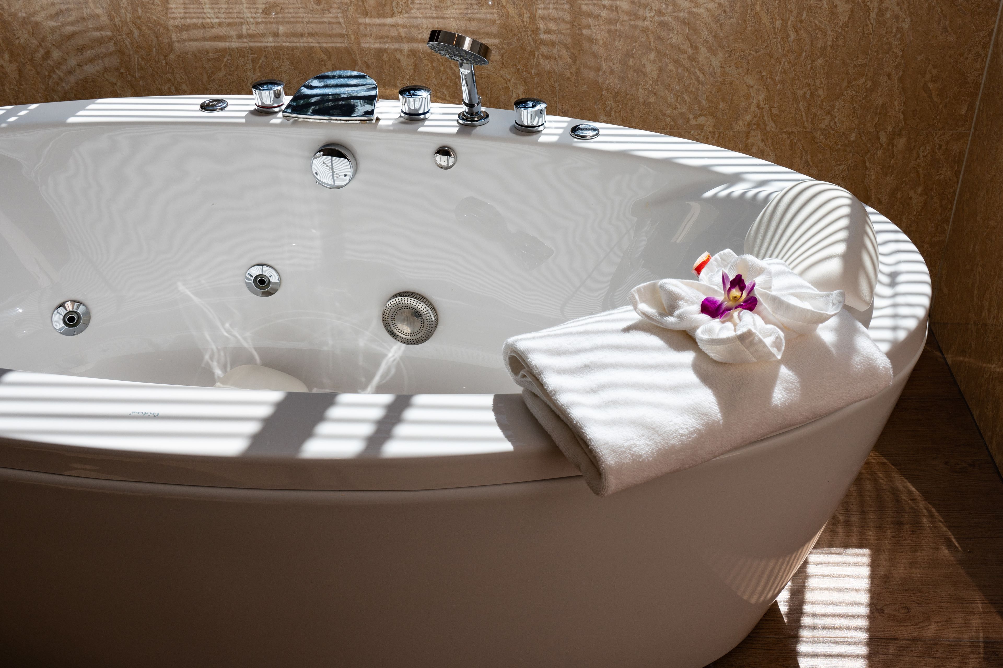 A modern bathtub with multiple faucets, a built-in showerhead, and a towel with an orchid.