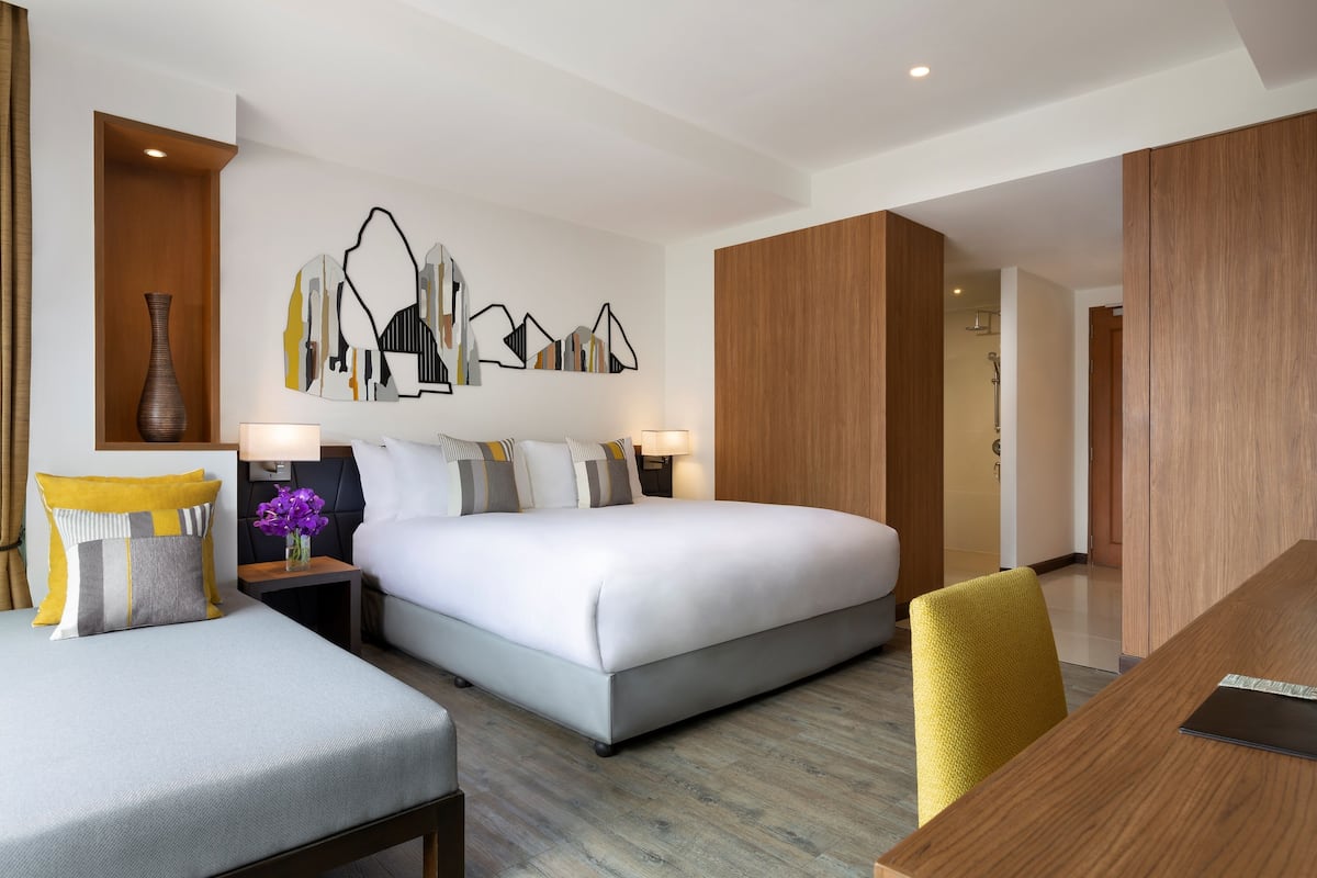 Habitación de hotel moderna con una cama grande, un escritorio y una silla. Hay una obra de arte en la pared sobre la cama y un florero en la mesita de noche.