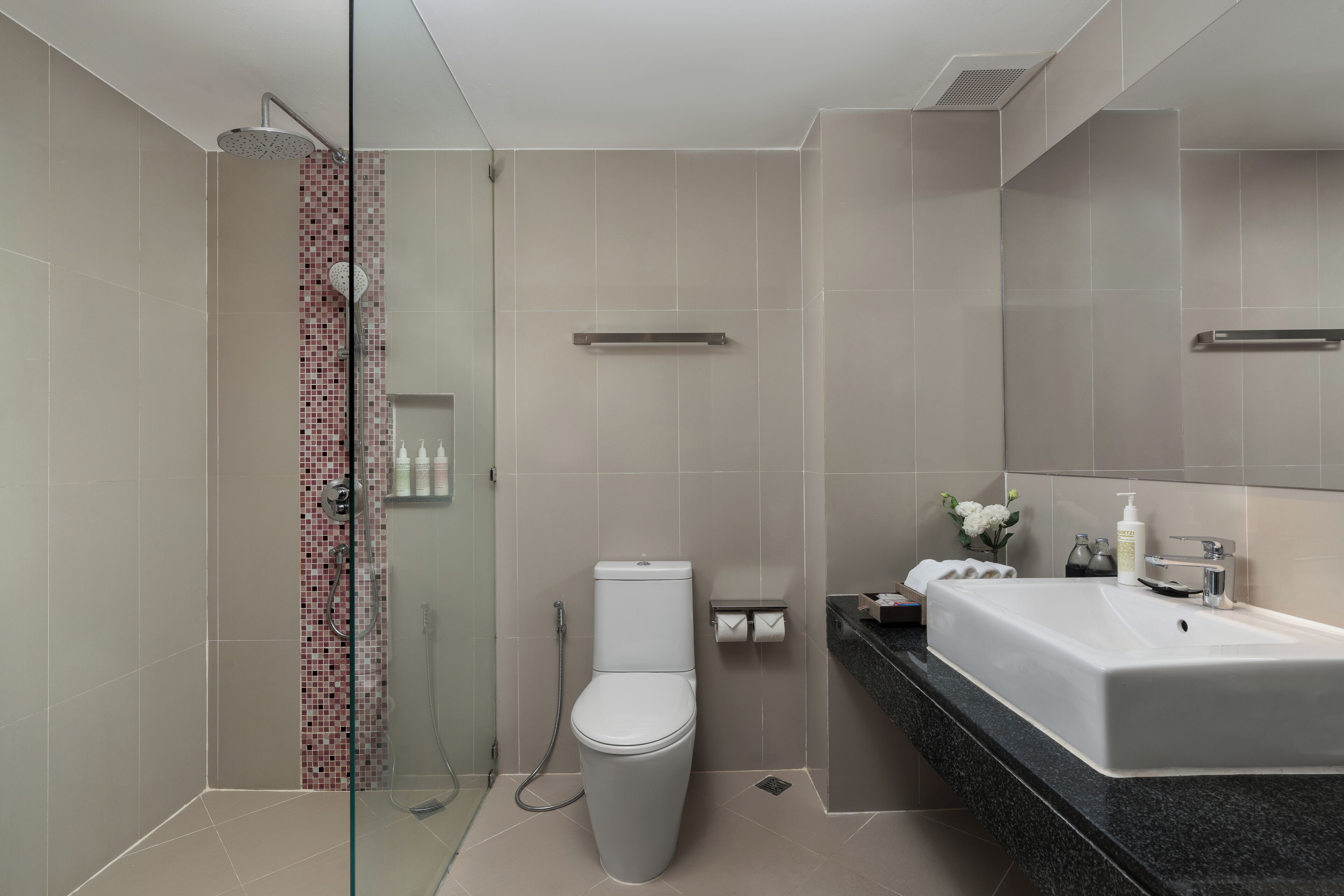 Un baño moderno con ducha envuelta en vidrio, inodoro y tocador con lavabo y espejo.