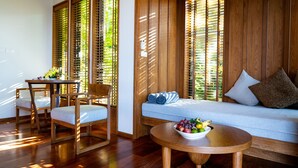 Een kamer met een houten vloer, een bank met kussens, een eettafel met stoelen en een schaal fruit op een bijzettafeltje.