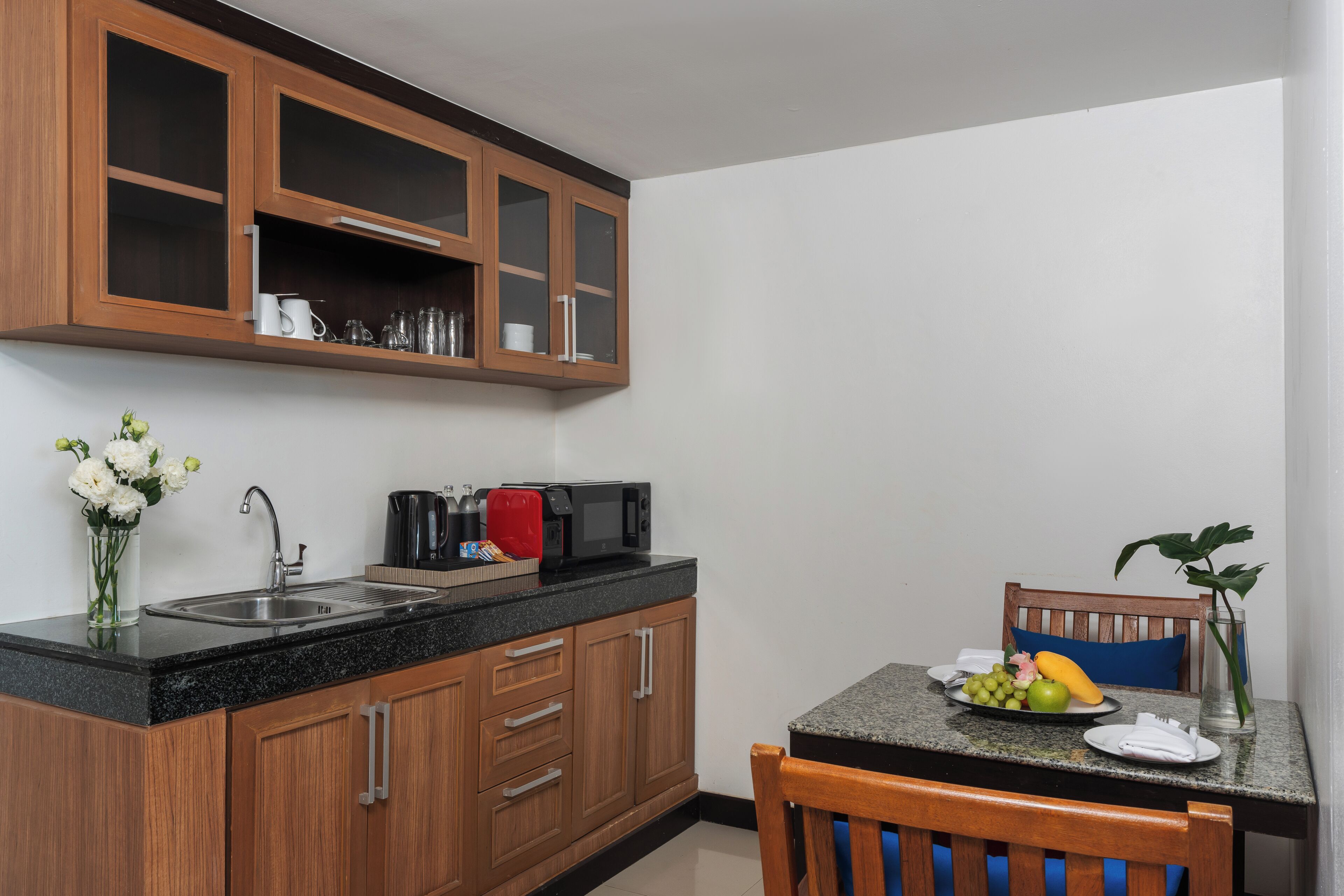 A compact kitchen with wooden cabinets, a granite countertop, a sink, and a dining area with a chair and table.