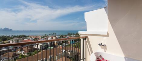 A balcony with a view of the sea, a white bathtub with rose petals, and a railing.