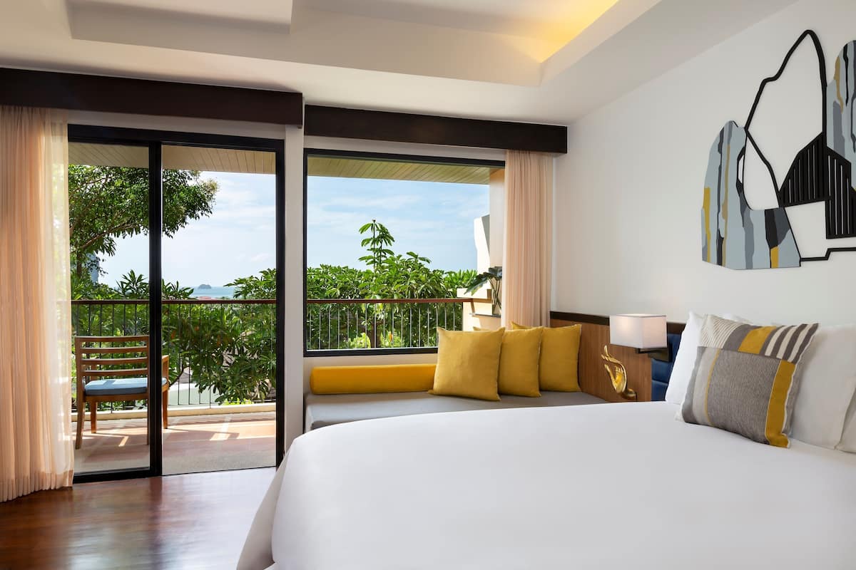 Habitación de hotel con una cama grande, un balcón con vistas a zonas verdes y una obra de arte moderno en la pared.
