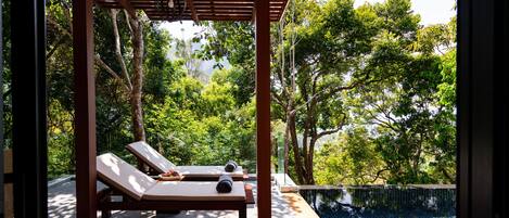 A covered outdoor area with two lounge chairs and a pool.