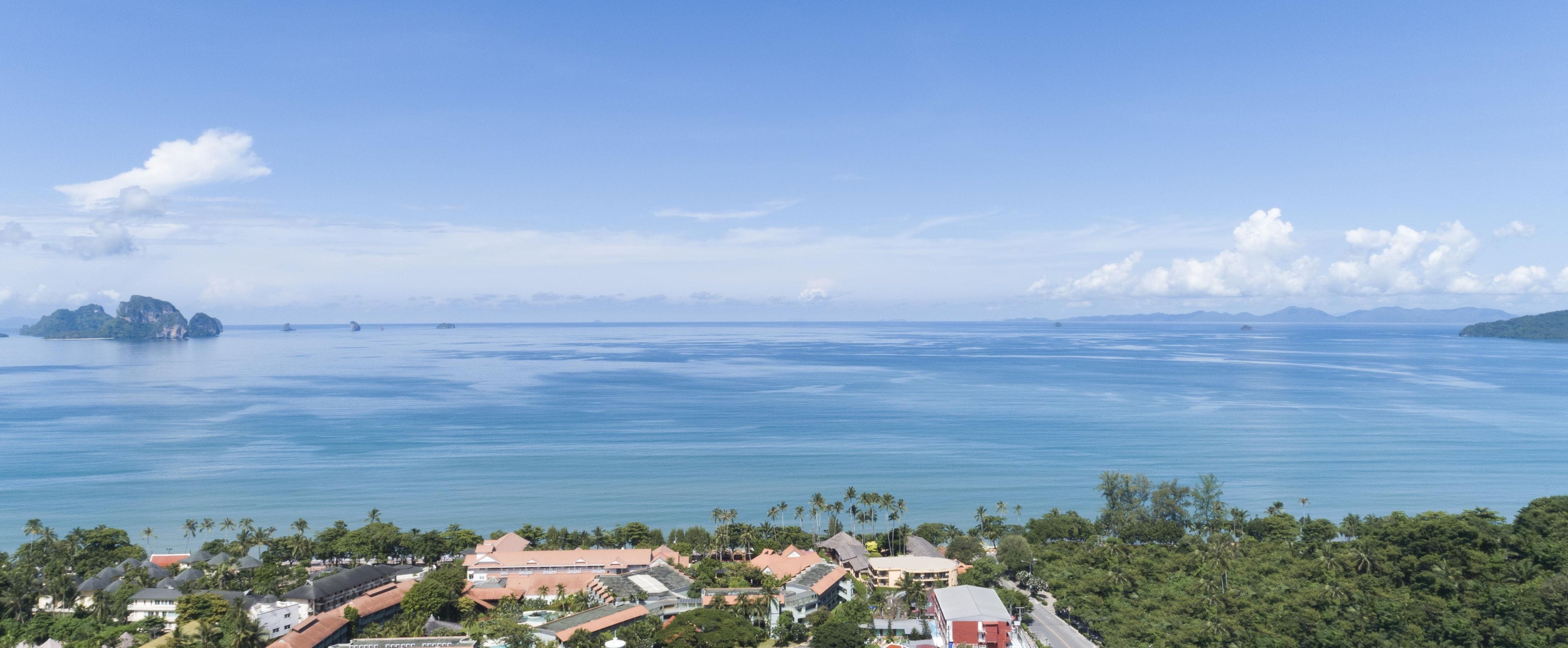 A coastal resort with multiple buildings, a clear view of the ocean, and palm trees.