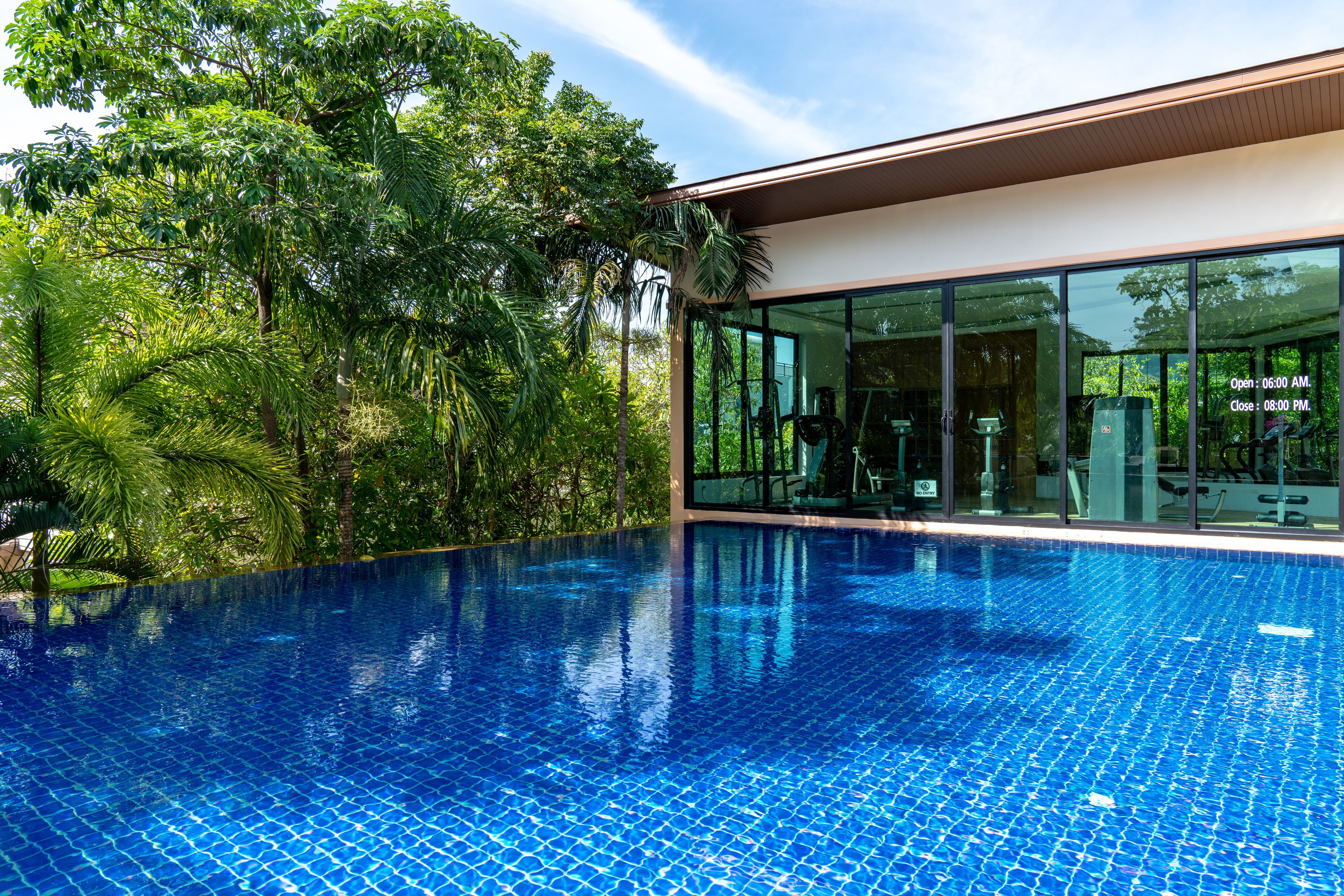 A swimming pool with a tiled blue surface, surrounded by lush greenery and a modern building with large glass windows.