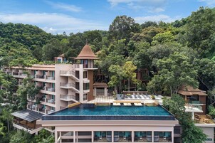 A hotel with a rooftop infinity pool, multiple balconies, and lush surrounding greenery.