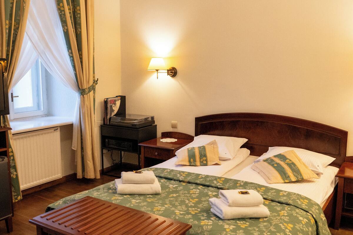A hotel room with a wooden bed, a bedside table, a lamp, and a window with curtains.