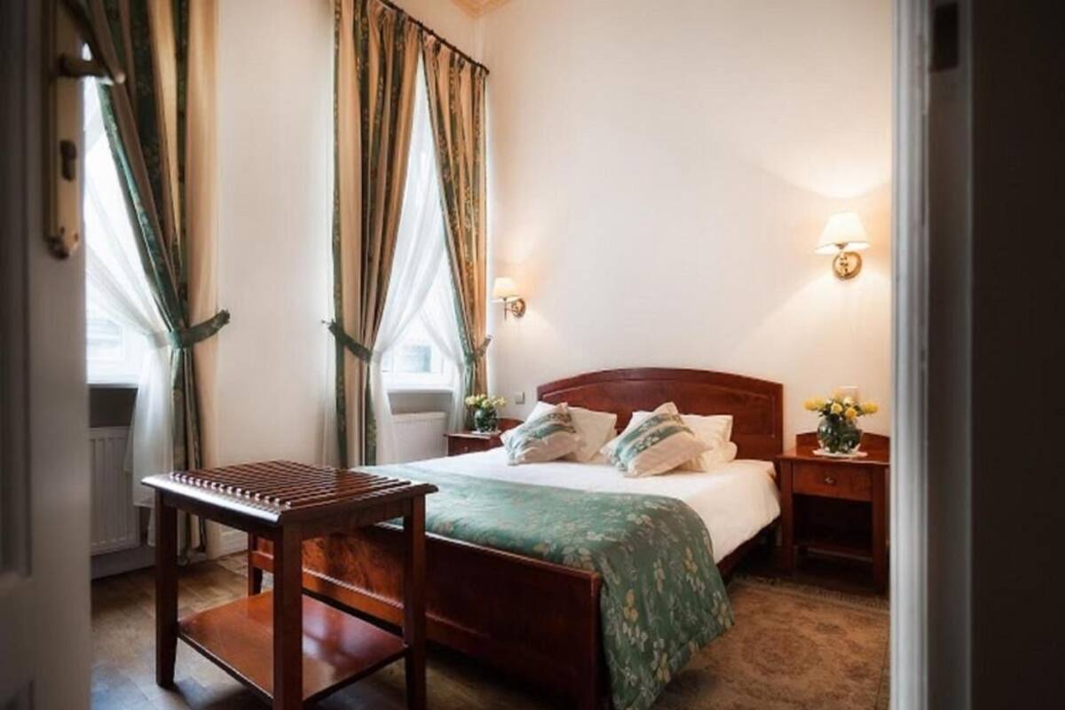 A bedroom with a wooden bed, a bedside table, a nightstand, and a window with curtains.