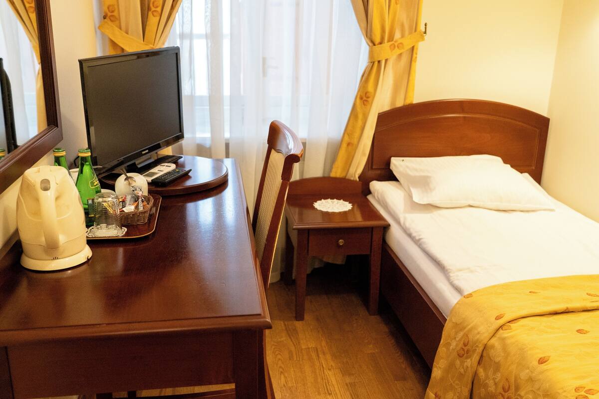 A hotel room with a wooden desk, a television, a bed with a white pillow, and a yellow bedspread.