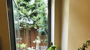 A breakfast table with various food items, a vase with flowers, and a view of a garden through a glass door. - Aparthotel Karmel (Kraków)