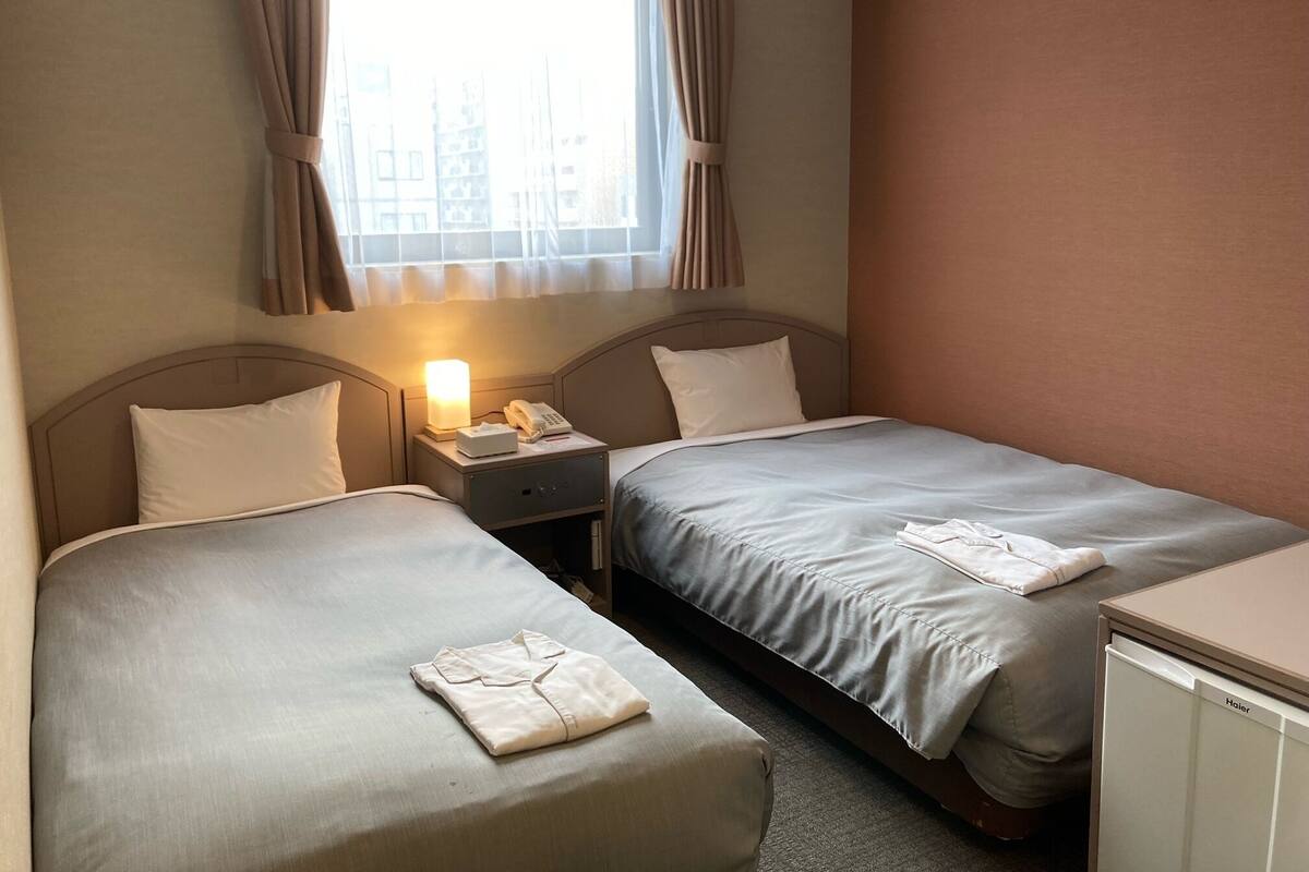 Quarto de hotel com duas camas, uma mesa de cabeceira com abajur, telefone e um pequeno armário.