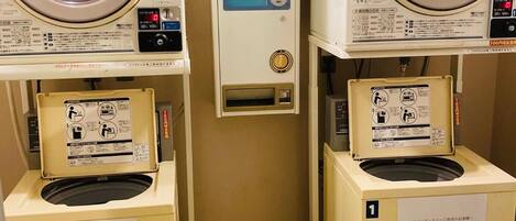 A laundry facility with two dryers and a washing machine, each with a control panel and a detergent dispenser.
