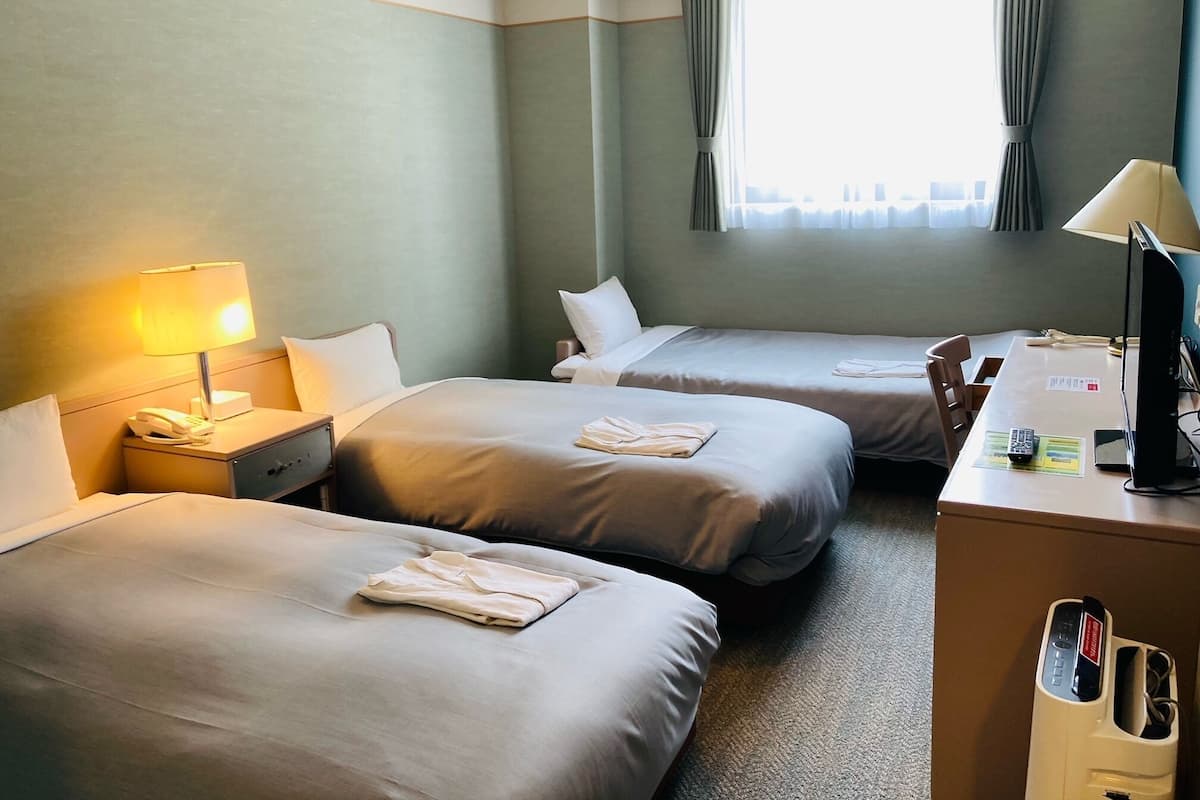 Quarto de hotel com duas camas, uma escrivaninha com computador, telefone e abajur.