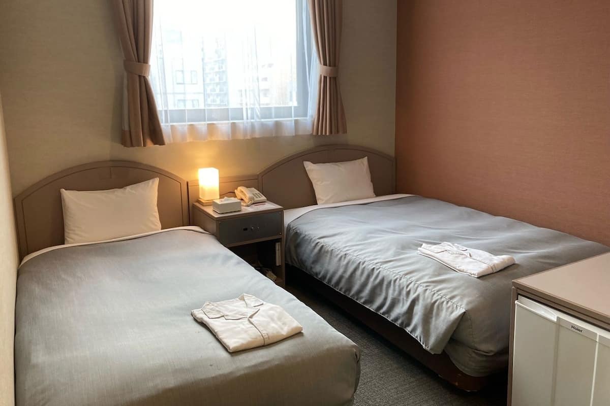Quarto de hotel com duas camas, mesa de cabeceira com abajur, telefone e um pequeno armário.