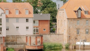 A water channel with a dam, buildings with red-tiled roofs, and a stone building with a balcony. - CASCADA Rheine by Hackmann (Rheine)