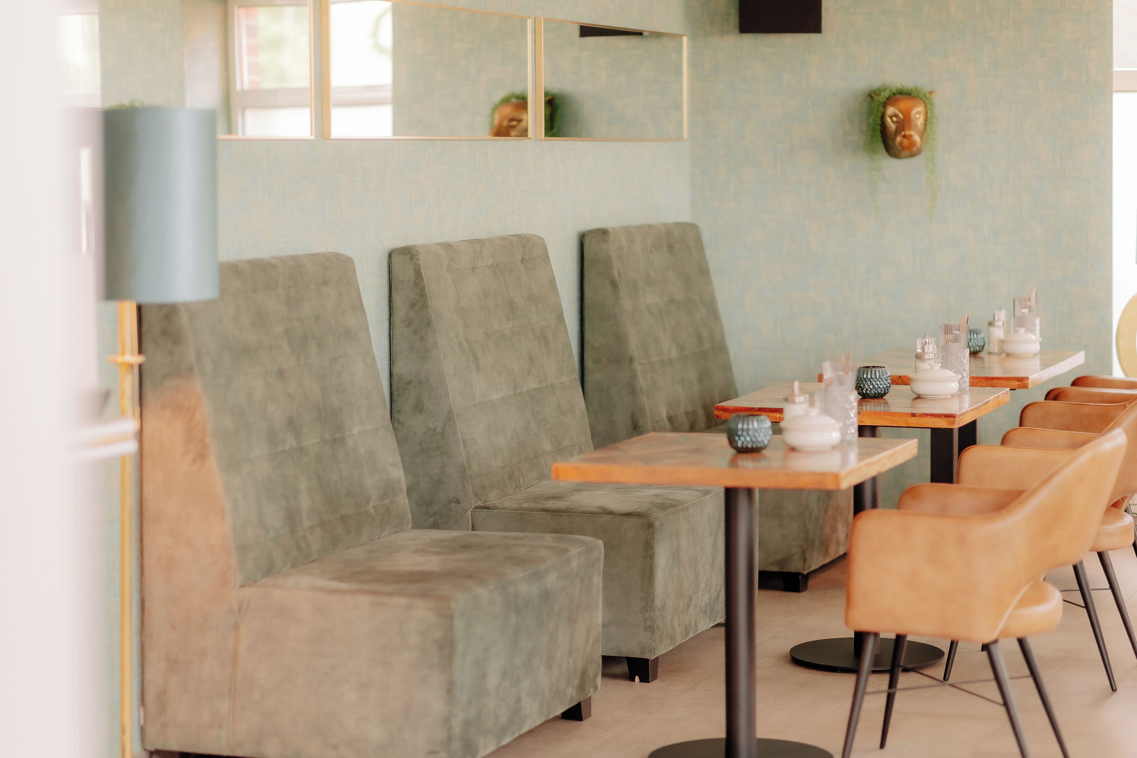 A modern interior with grey upholstered seating, wooden tables, and a mirror reflecting the room.