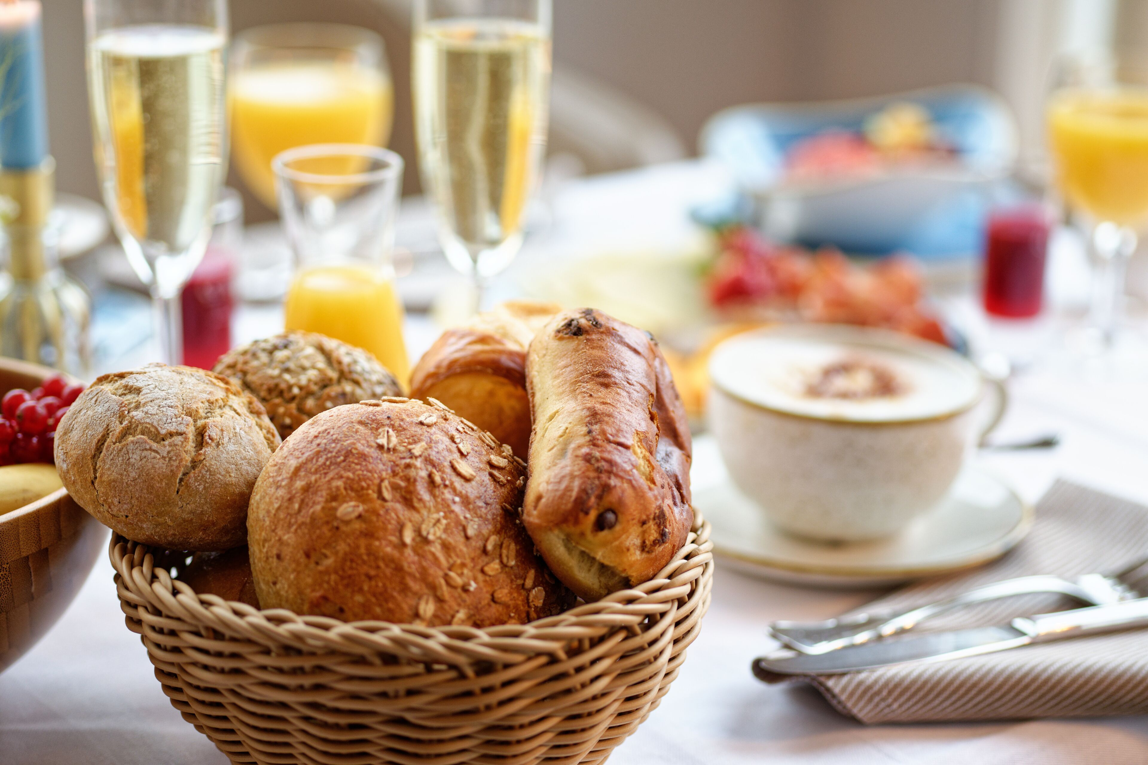 A wicker basket filled with various breads, a bowl of soup, and a cup of coffee on a table with a napkin and utensils.