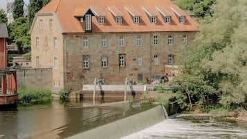 A historic building with a stone facade and a red-tiled roof, situated beside a water channel.
