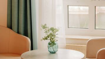 A room with a bed, a round table with a vase, a sofa, and a window with curtains.