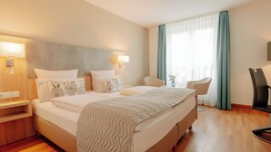 A hotel room with a large bed, two bedside tables, a chair, a desk, and a window with curtains. - CASCADA Rheine by Hackmann (Rheine)