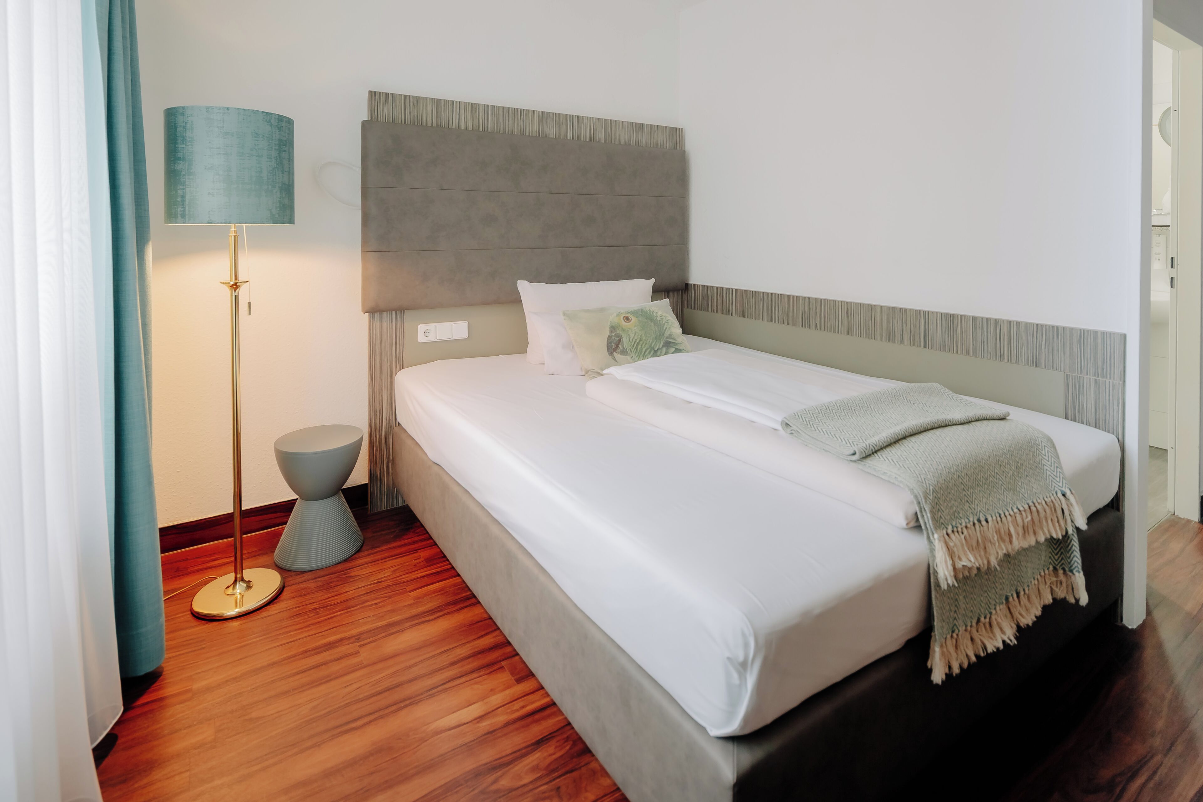 A hotel room with a bed, a lamp, a bedside table, and a wall-mounted headboard.