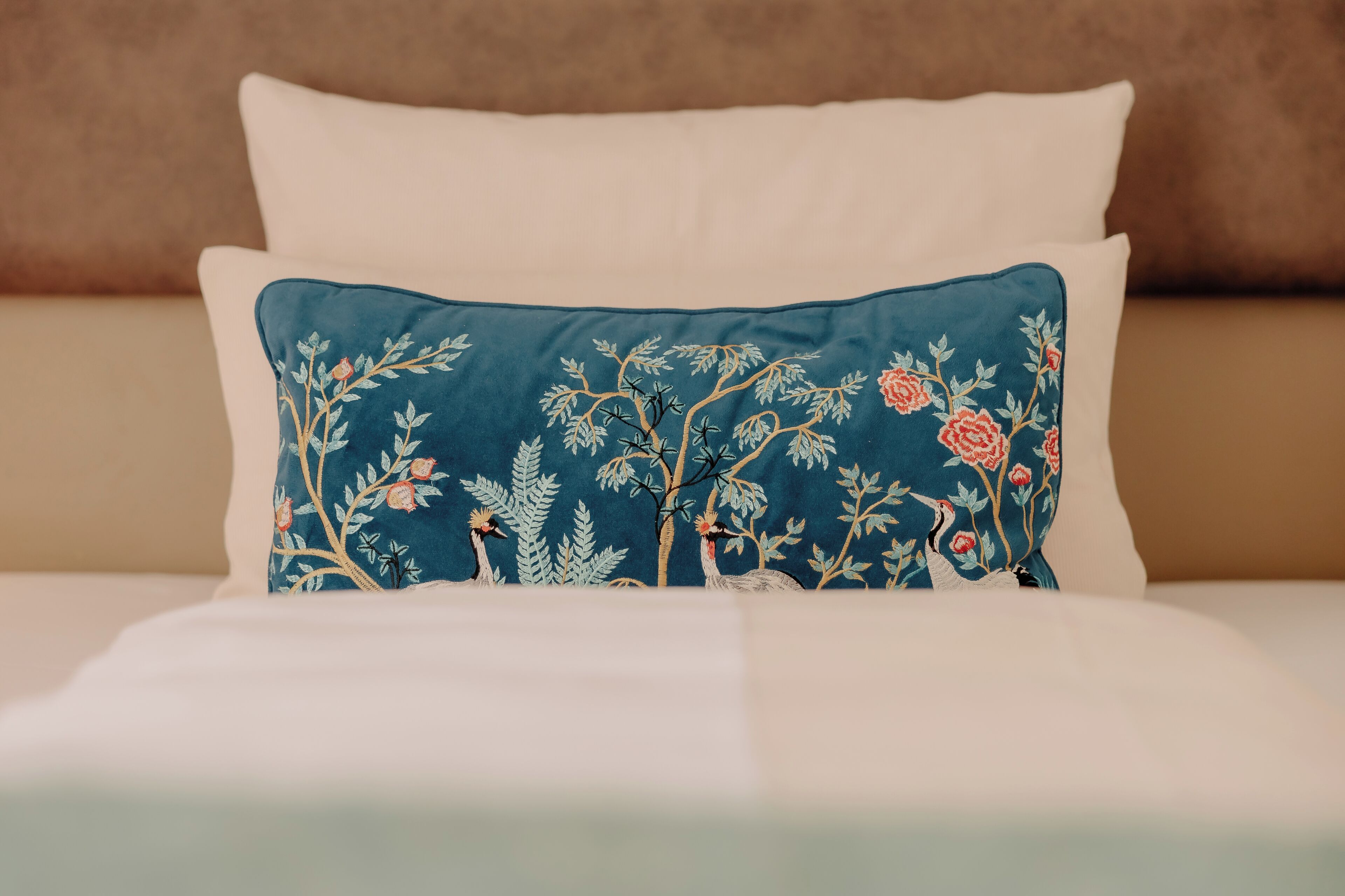 A bed with a blue pillow featuring floral embroidery and a white pillow.