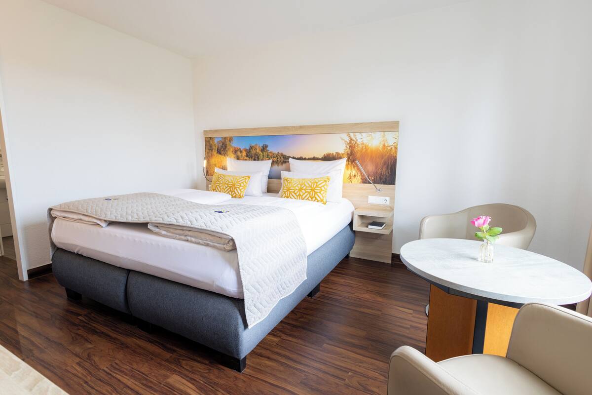 A hotel room with a bed, a bedside table, a chair, and a round table.