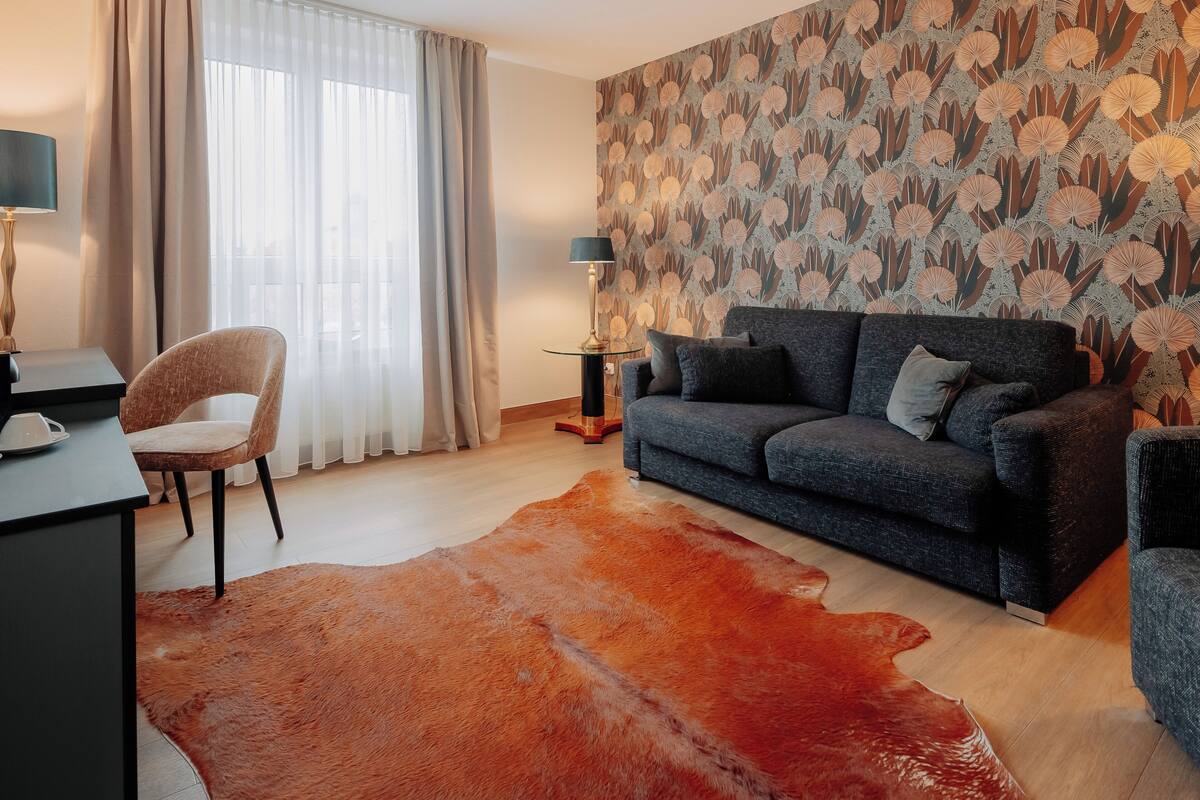 A modern living room with a sofa, a chair, a lamp, and a patterned wall.