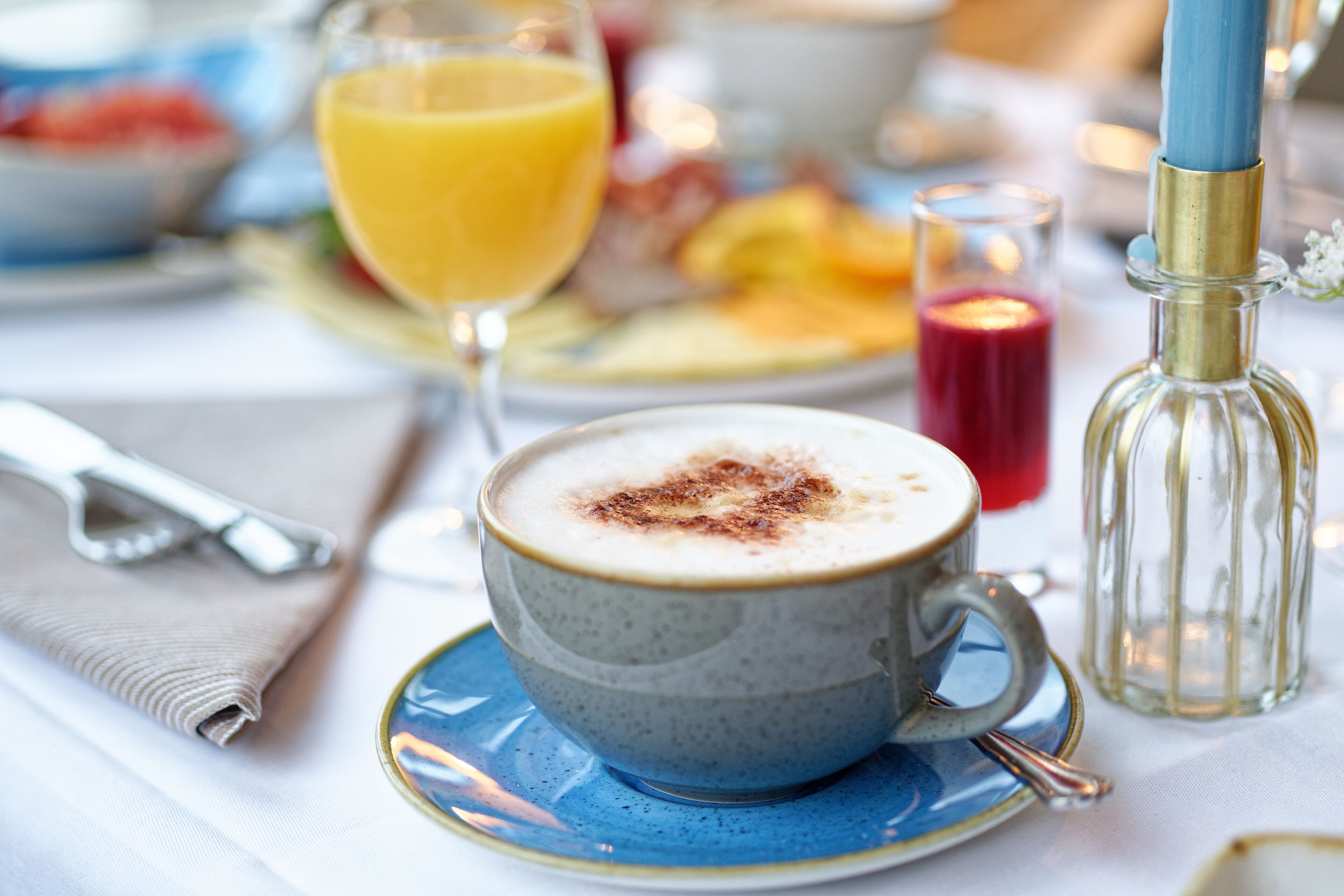 Un desayuno con una taza de café, un vaso de zumo de naranja y una vela sobre la mesa.