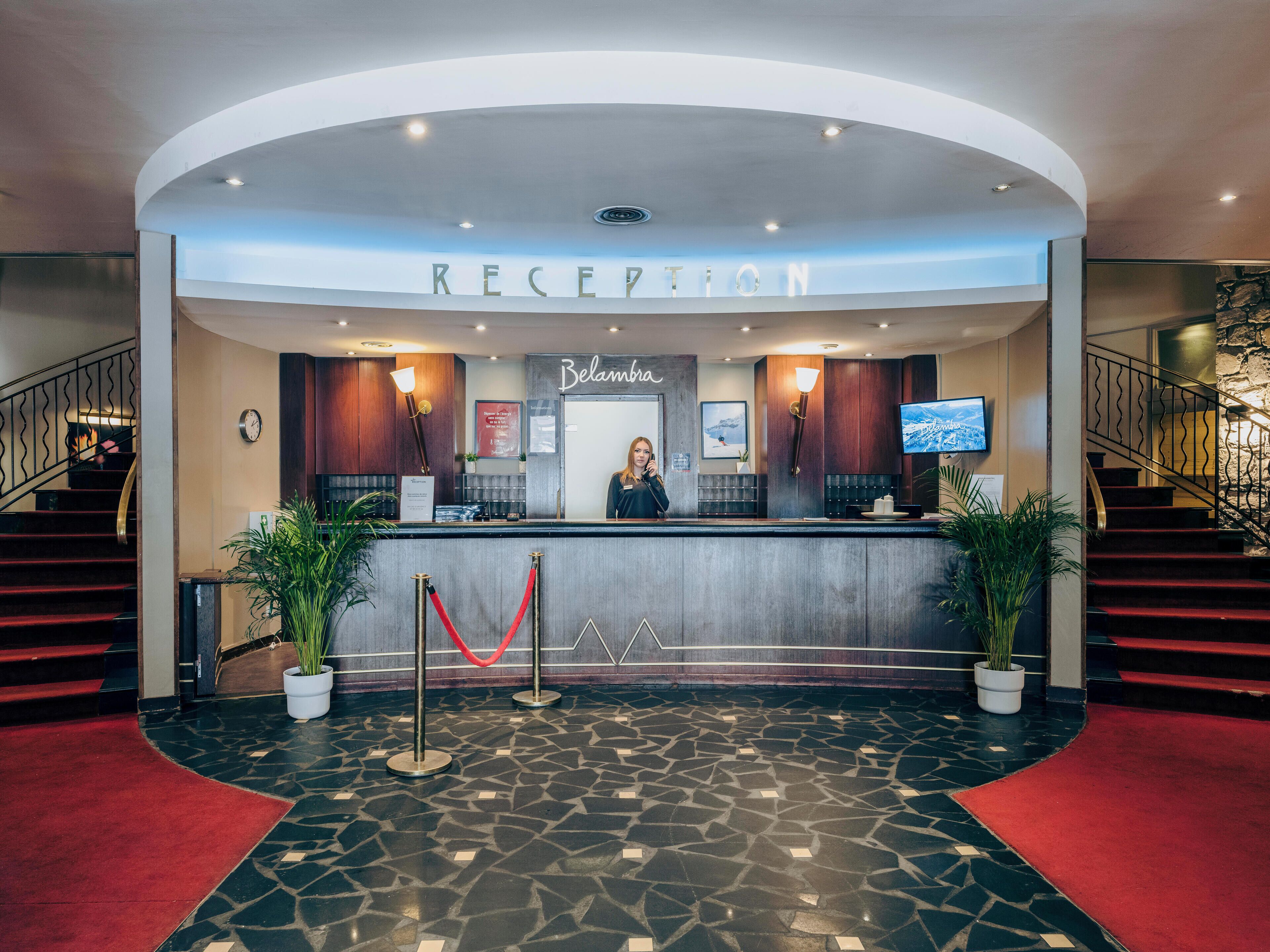 A reception area with a receptionist, a clock, a sign reading "Belambra," and a staircase.